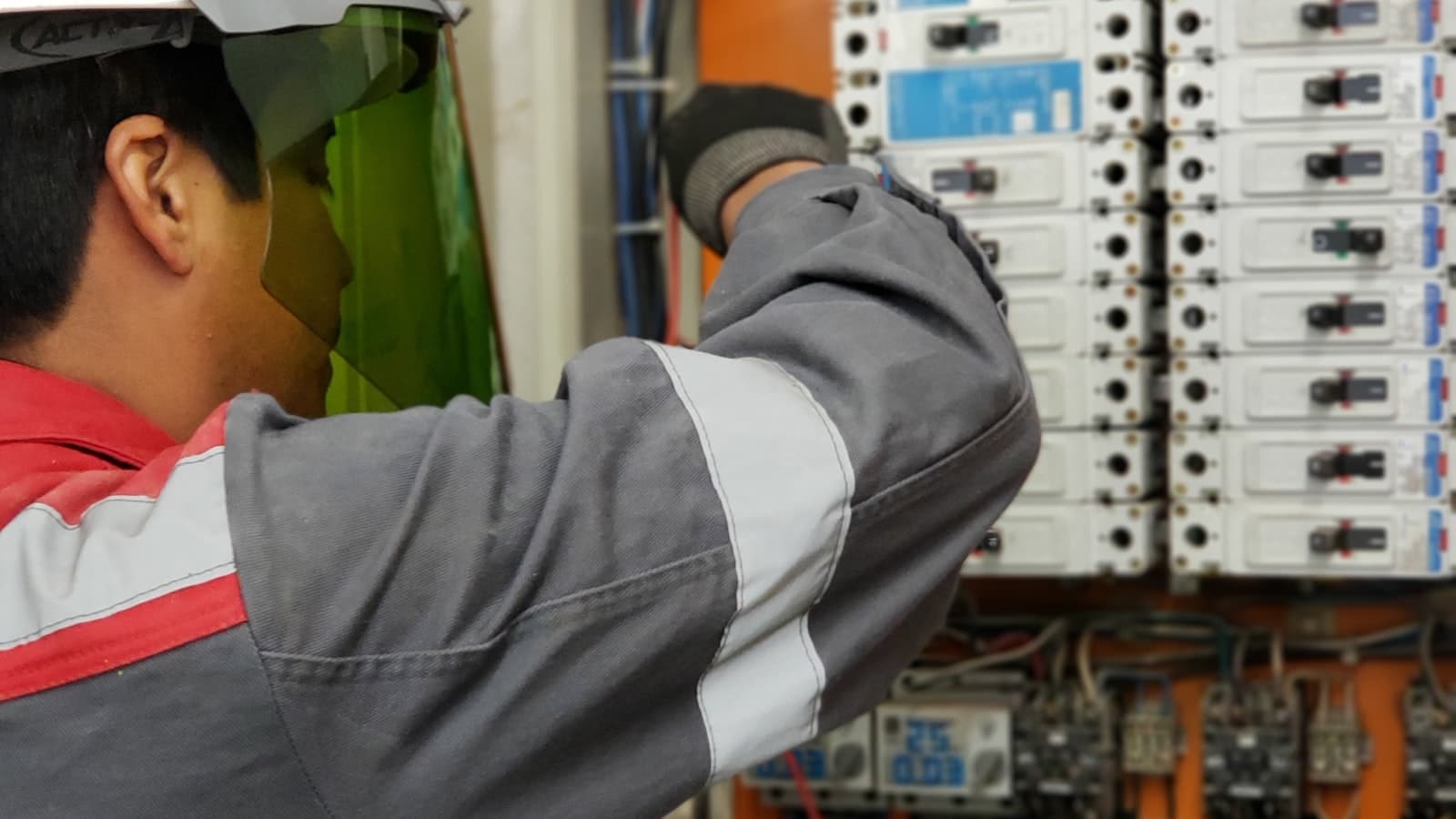 An electrician in safety gear working inside an industrial breaker panel