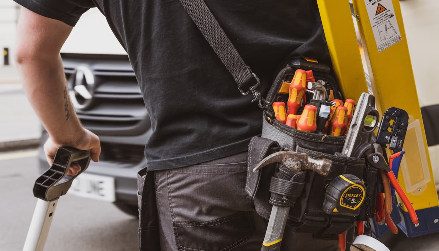An HVAC technician arriving at a job with a tool belt and ladder