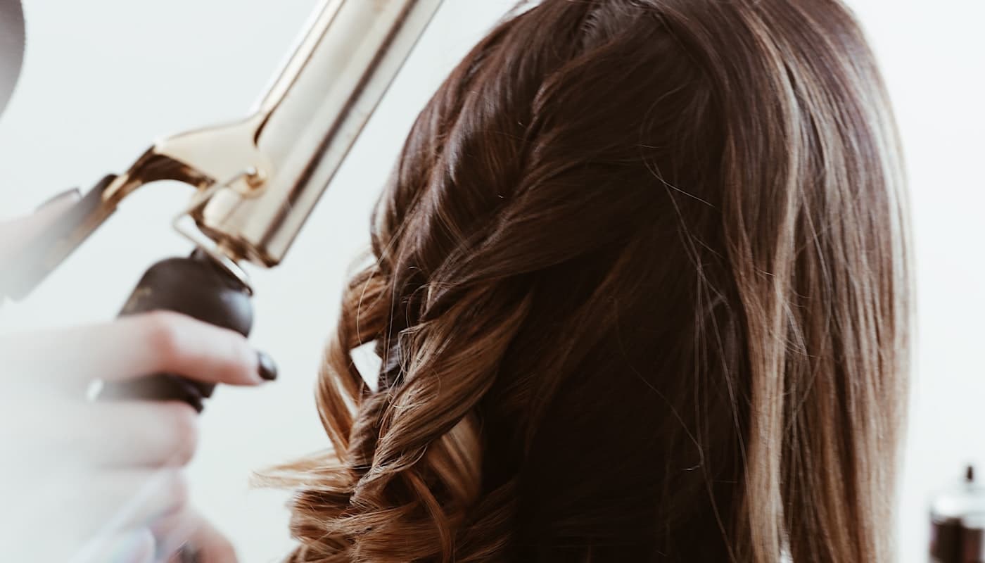 A stylist using a curling iron on a client's long hair