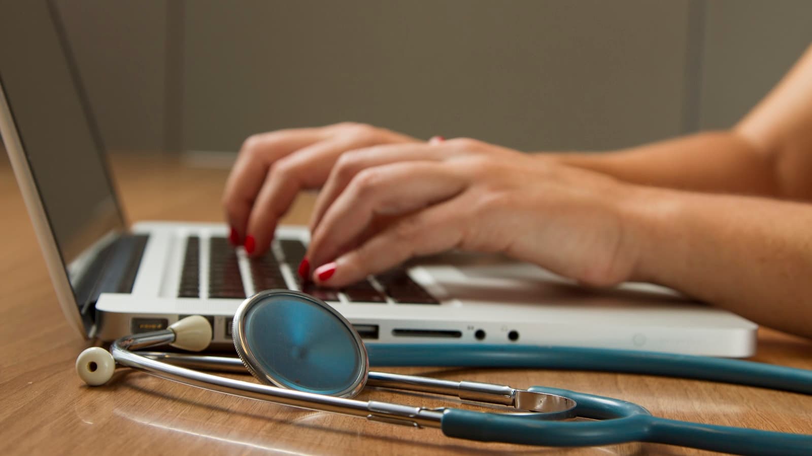 A clinic worker booking an appointment at a laptop beside a stethoscope