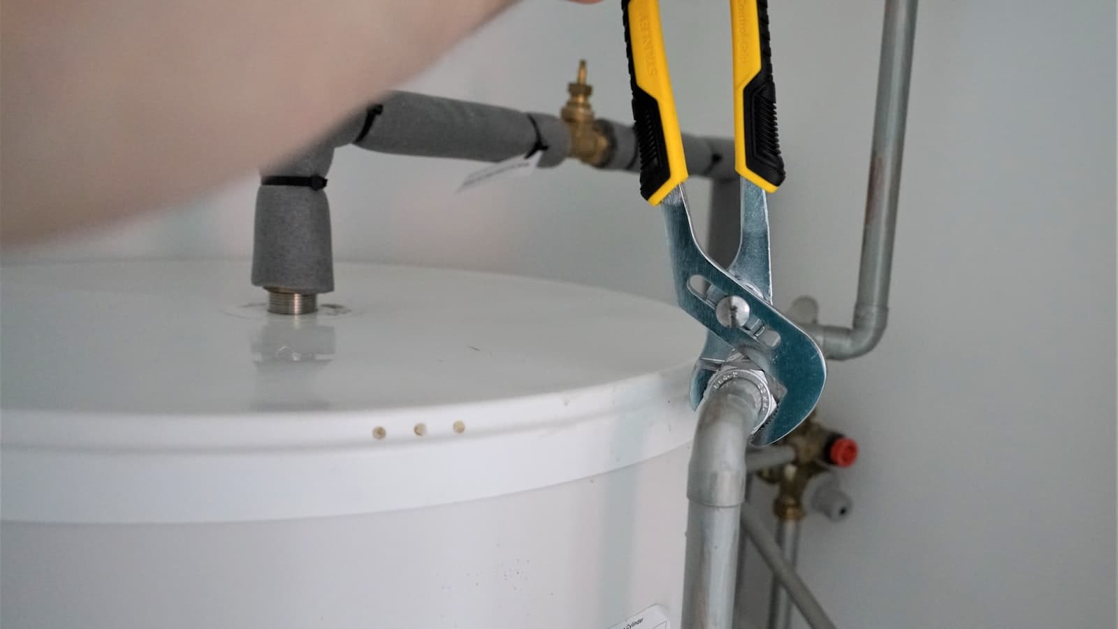 A plumber tightening a fitting on a water heater with slip-joint pliers