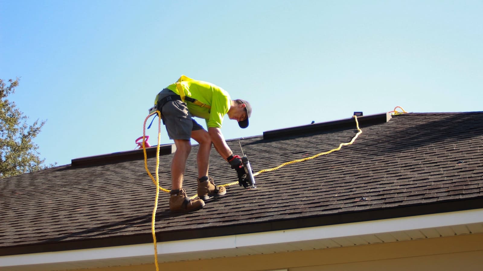 A roofer fastening shingles on a sloped roof under a blue sky